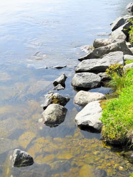 Bank of the river with stones on blue sky background