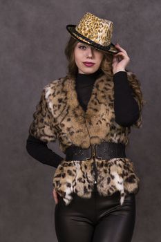 Girl model in fur coat and Leopard Hat posing on grey background in the Studio.