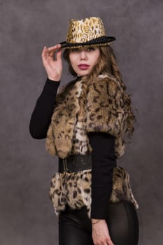 Girl model in fur coat and Leopard Hat posing on grey background in the Studio.