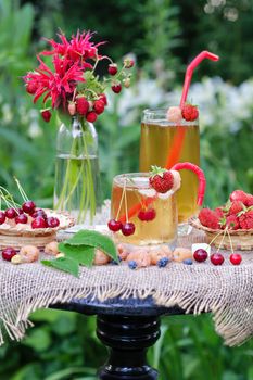 Iced tea and different berries on the table in the garden.