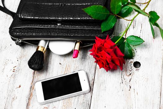 Women bag with lipstick,powder and cosmetics and a bright red rose