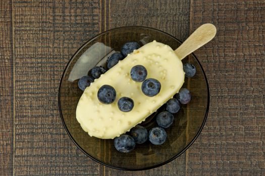 Vanilla ice cream on a stick with cranberries on a plate one standing on an old wooden counter in vintage style.Flat,horizontal view.