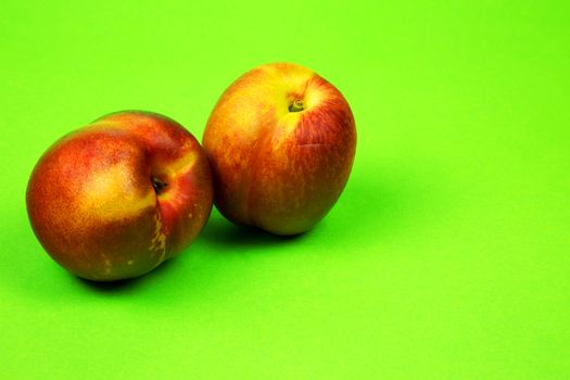 Two fresh nectarines on a light green cardboard, slightly grainy background. Close , horizontal view.