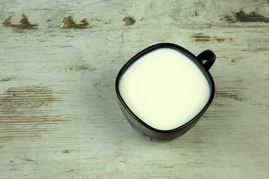 Black full cup of milk on a light, old wooden table in vintage style. Flat, horizontal view.