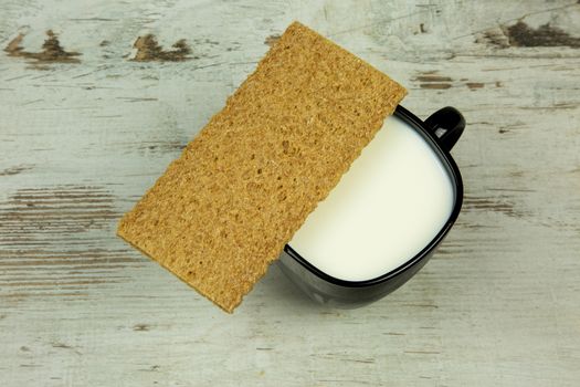 Cup of milk and crispy bread on a old,vintage wooden table. Flat,horizontal view.