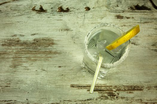 Glass from the shores of decorative sugar, full of cold water with ice and lemon, refreshing drink for the summer on an old wooden table in vintage style with space for text. Flat, horizontal view.