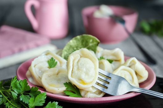 Dumplings on a plate and a fork, gray-blue background, rustic style. Utensils and napkins in the background, low key and bokeh.