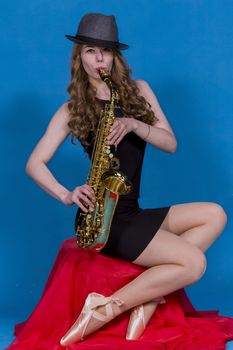 girl in Pointe and saxophone on a red silk on a blue background in the Studio