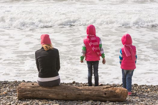Two girls and a girl on the beach sitting on a log and looking into the distance