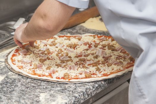 Man chef with raw pizza. Young male in uniform preparing pizza on table.