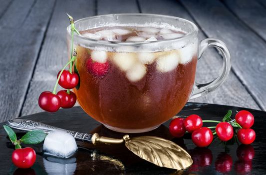 Iced tea with berries and ice, vintage spoon and gray background of boards