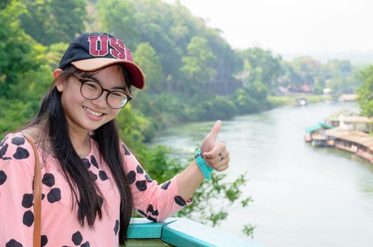 Tourist girl show thumb appreciate the beautiful landscape of Death Railway bridge over the Kwai Noi River at Krasae cave viewpoint in Kanchanaburi province, Thailand 