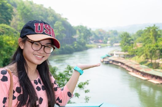 Tourist girl show hands invites to visit beautiful landscape of Death Railway bridge over the Kwai Noi River at Krasae cave viewpoint in Kanchanaburi province, Thailand