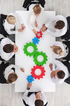 Business team sitting around the table with cogs, teamwork concept