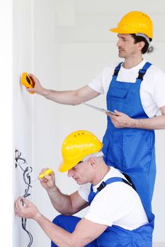 Two builders in helmets working with electricity indoors