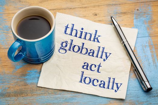 Think globally, act locally reminder - handwriting on a napkin with a cup of espresso coffee