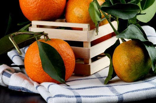 Fresh Ripe Tangerines with Leafs in Wooden Box  closeup on Napkin on Dark Wooden background