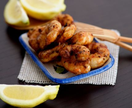 Delicious Grilled Prawns on Small Plate with Sliced Lemon and Wooden Forks closeup on Wooden Cutting Board. Selective Focus