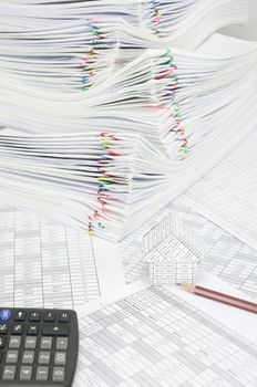 House and pencil on finance account have blur calculator and pile paperwork of report with colorful paperclip as background.