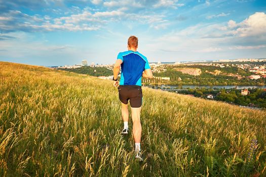 Sport lifestyle. Athletic young man is running on the hillside outside the city. Prague, Czech Republic.
