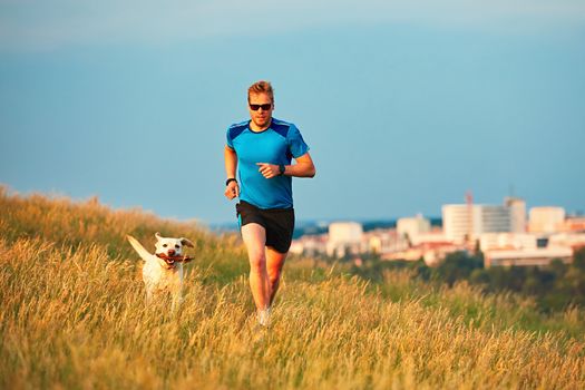 Sport lifestyle with dog. Athletic young man and labrador retriever are running on the hillside outside the city. Prague, Czech Republic.