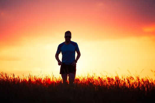 Silhouette of runner. Outdoor cross-country running. Athletic young man is running in the nature during golden sunset.
