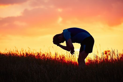 Silhouette of runner. Outdoor cross-country running. Pensive young man is taking rest after running in the nature during golden sunset.