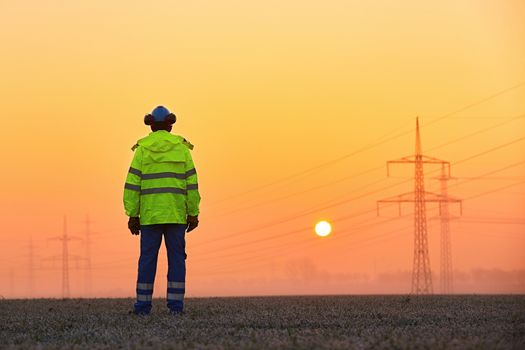 Worker is watching electricity pylons and substation at the sunrise