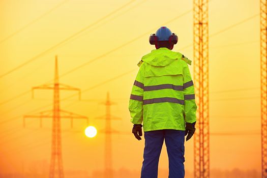 Worker is watching electricity pylons and substation at the sunrise