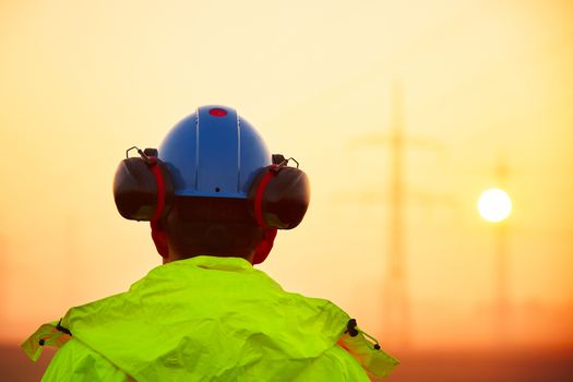 Worker is watching electricity pylons and substation at the sunrise