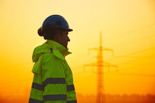 Worker is watching electricity pylons and substation at the sunset