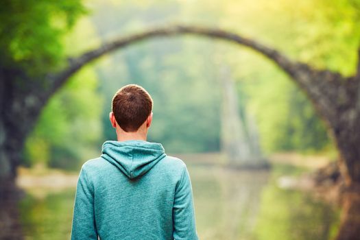 Pensive young man on the pond bank. - Amazing place in Germany. Rakotzbrucke also known as Devils Bridge in Kromlau. 