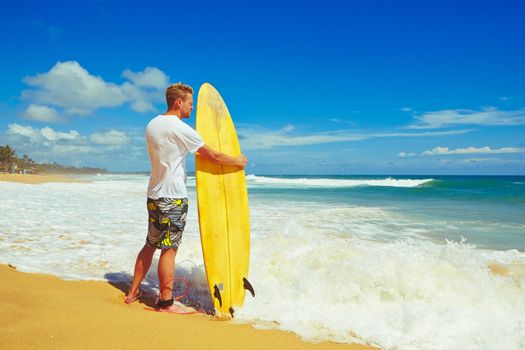 Man with surfboard on the beach at sunset.