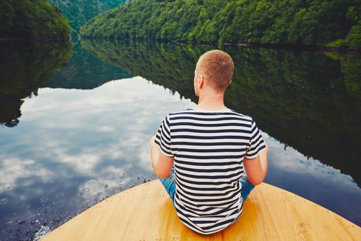 Vacation trip on the river. Handsome man is sitting on the prow of the boat. 