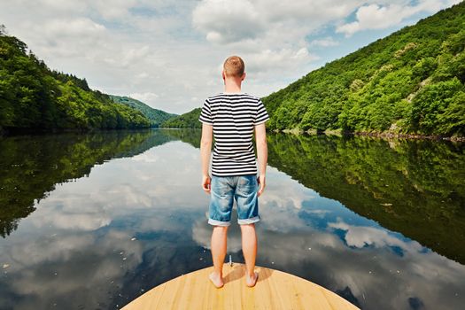 Vacation trip on the river. Handsome man with blue and white striped shirt on the prow of the boat. Vltava river near Prague, Czech Republic