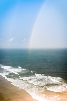 A colorful rainbow after a thunderstorm over crashing beach waves.