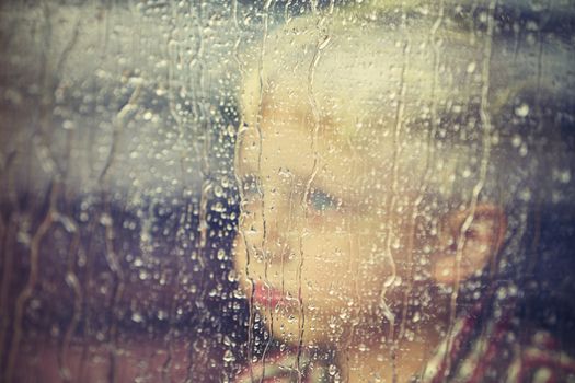 Little boy behind the window in the rain - selective focus