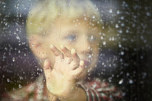 Little boy behind the window in the rain - selective focus