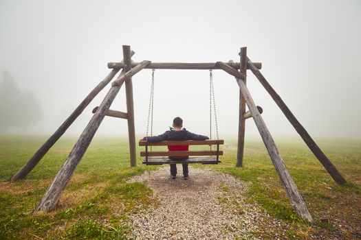 Sad man on the swing in mysterious fog