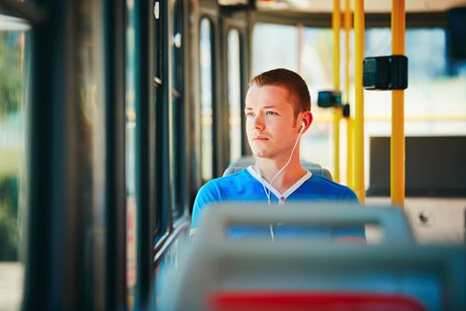 Loneliness man is wearing headphones and listening to music. Everyday life and commuting to work by public transportation. Handsome young man is traveling by tram. 