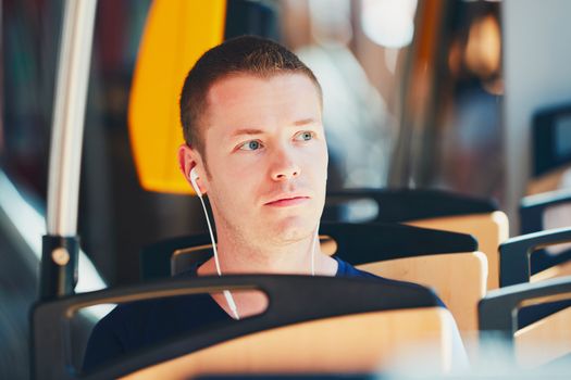 Everyday life and commuting to work by public transportation. Handsome young man is traveling by tram. Man is wearing headphones and listening to music.