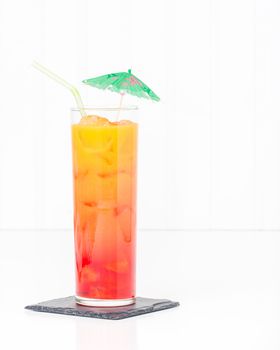 Tropical cocktail known as a tequila sunrise in a tall glass with ice.