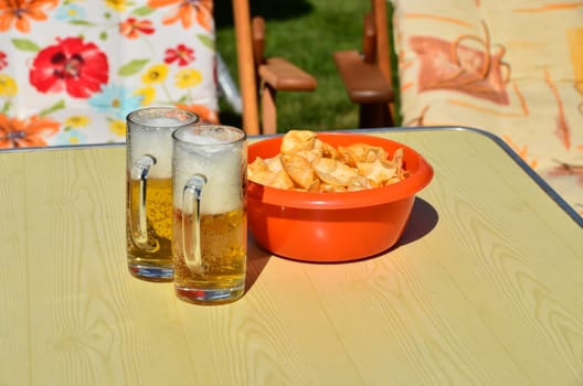 A glass of beer and a bowl of crisps on a table in the garden.