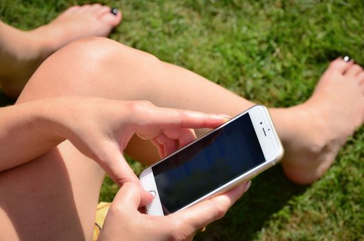 Women playing mobile phone in the garden during sunny day.