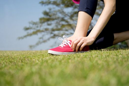 Running shoes - closeup of woman tying shoe laces on her barefoot running shoes. Female sport fitness runner getting ready for jogging outdoors.