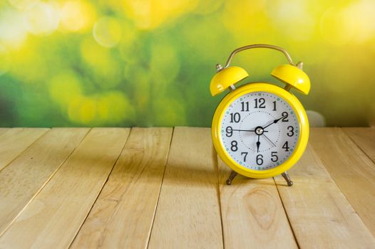 Yellow clock on wood table on bokeh blackground. Morning.