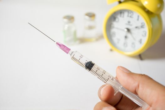 Hand holding syringe with clock.