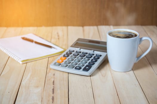 A cup of coffee on the table with calculator and notebook.