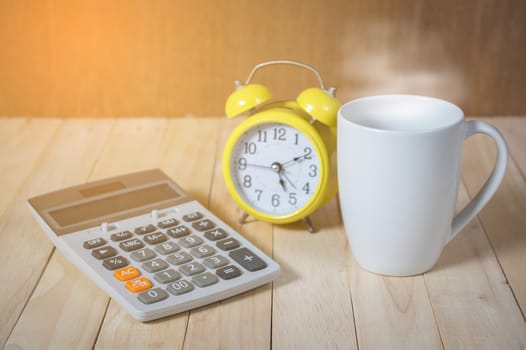 A cup of coffee on the table with calculator and clock.