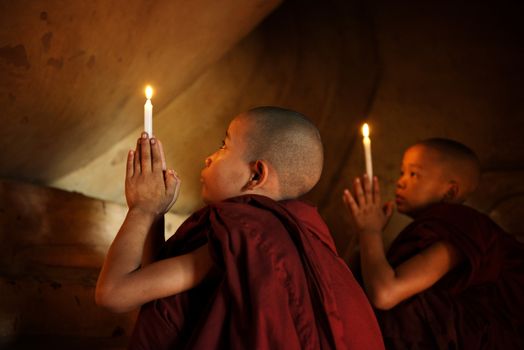 Little novice monks praying in front candlelight